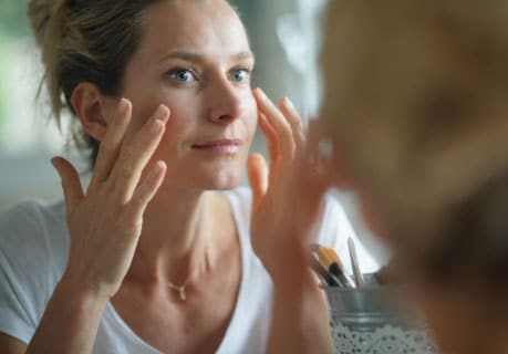 A middle-aged caucasian woman examines her face in the mirror