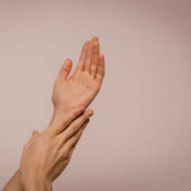 A person's hands reach up towards the sky and one caresses the wrist of the other
