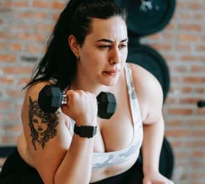 A plus-sized woman lifts weights at a gym in a sports bra