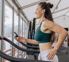 A strong lean woman runs on a treadmill with a smile on her face
