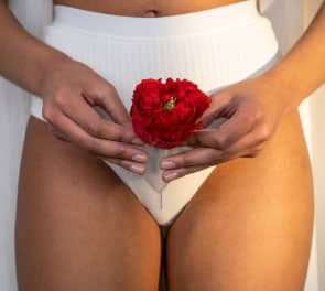 A woman in white underwear holds a menstrual cup with a red flower in it in front of her intimate areas
