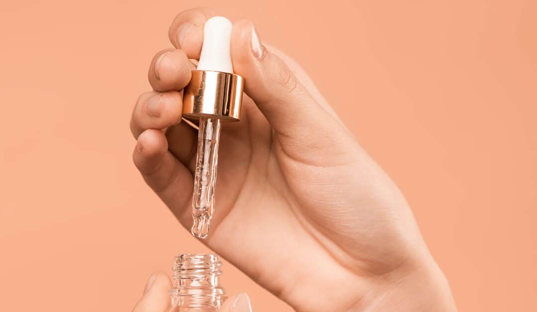 A woman's hand holds up a dropper filled with a skin hydrating serum