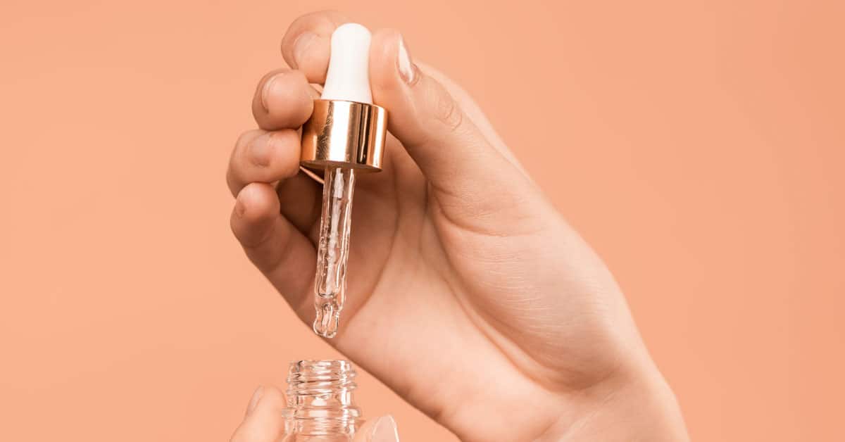 A woman's hand holds up a dropper filled with a skin hydrating serum