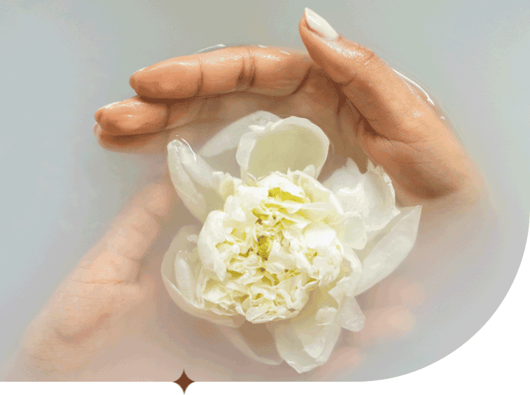A woman's hands delicately cup a blossoming flower floating in bathwater