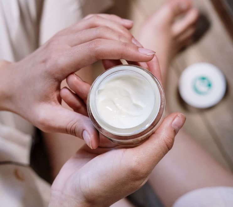 A woman's hands hold an open jar of skin cream