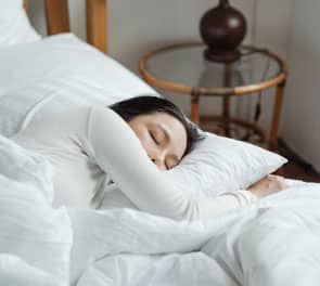 An Asian woman sleeps in a comfortable looking bed