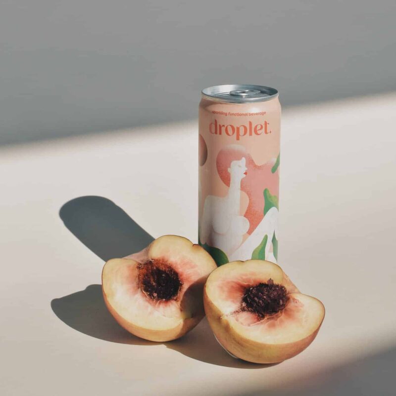 Canned drink, label reads Droplet, halved peach sits in front of the can