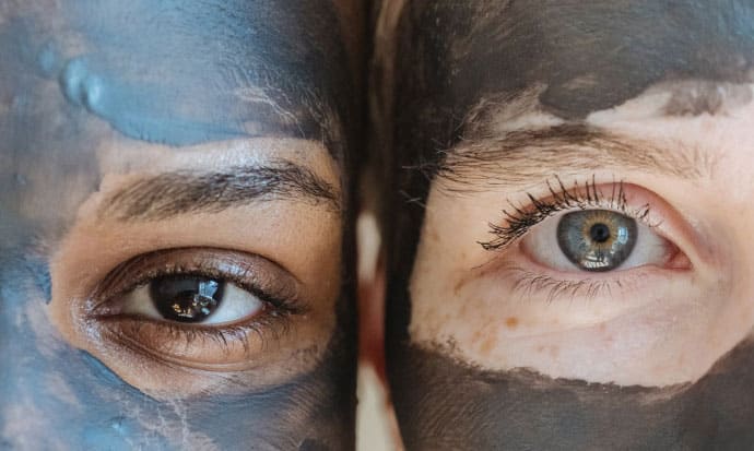 Closeup of two people's faces showcasing their eyes and surrounding skin in a charcoal mask