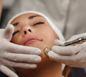 Gloved hands performing microdermabrasion facial on young woman's chin