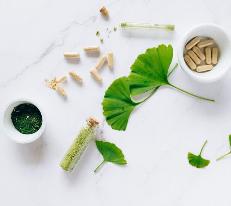 Supplement capsules laid out aesthetically with plant leaves and powders