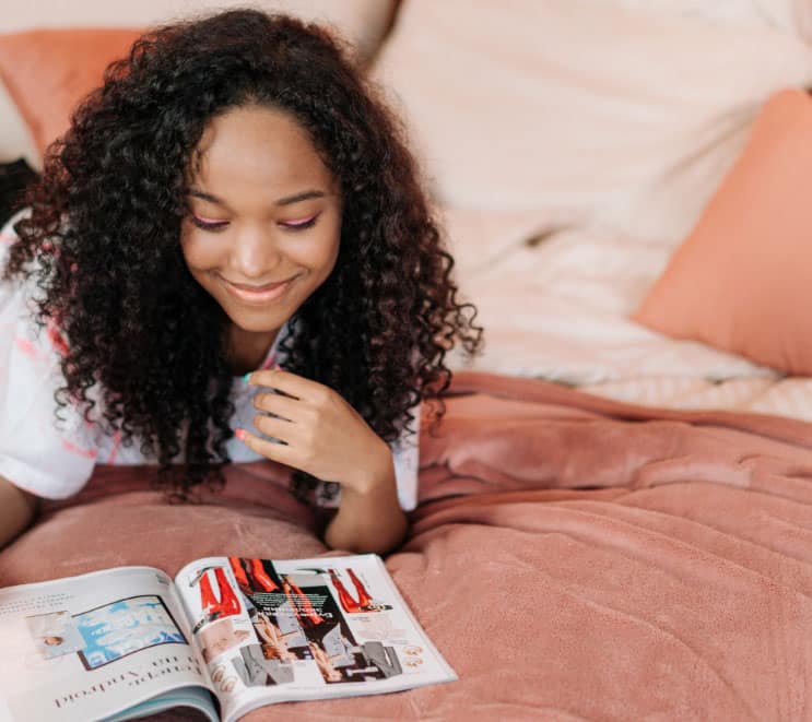 Teenage girl lays in her bed looking at magazines, life coaching