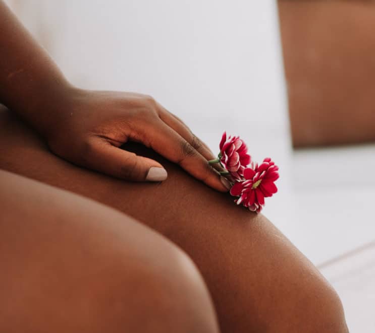 Woman holds a flower and rests her hand on her bare legs, thermiva