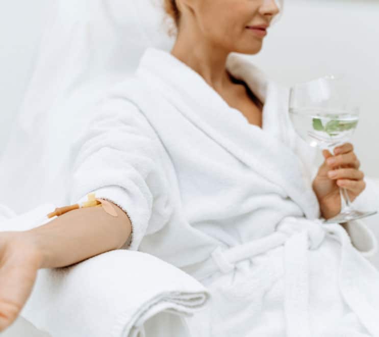 Woman sips lemon water in a robe while she goes through IV infusion therapy
