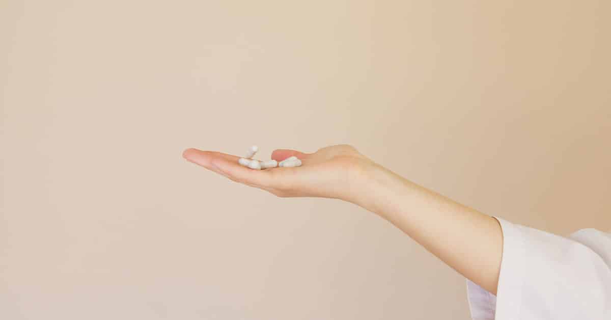 Outstretched hand on neutral background holds a handful of pills, Bioidentical Hormone Replacement Therapy