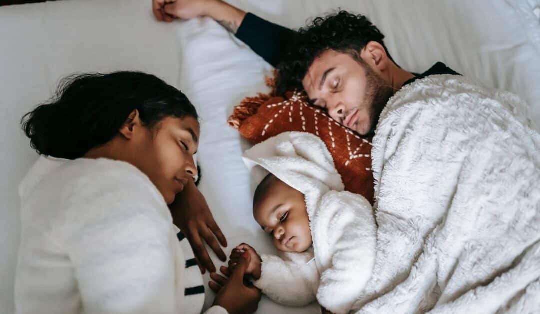 A mother, father, and child sleep together in clean cozy bedding