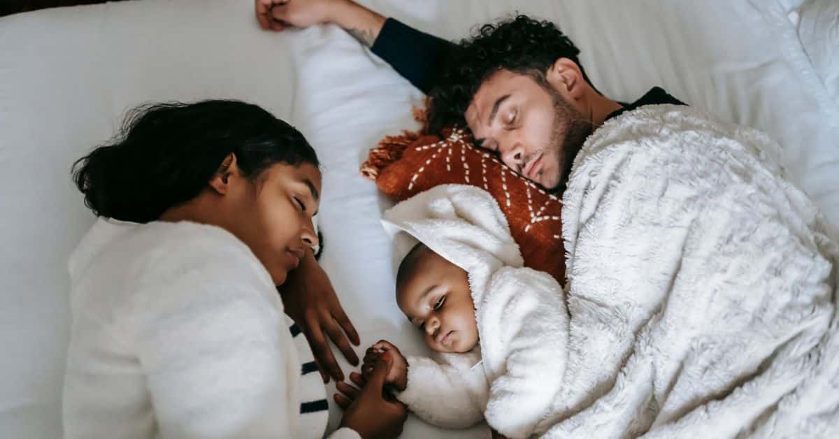 A mother, father, and child sleep together in clean cozy bedding