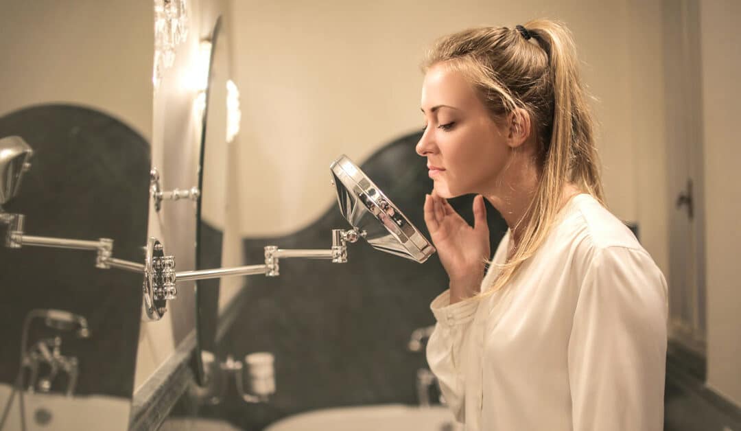 A woman examines her face with a magnifying mirror, Guide to Chemical Peels