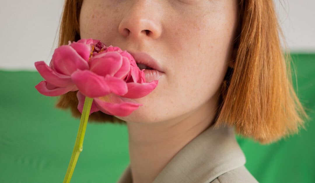 A woman holds a flower up to her pursed lips