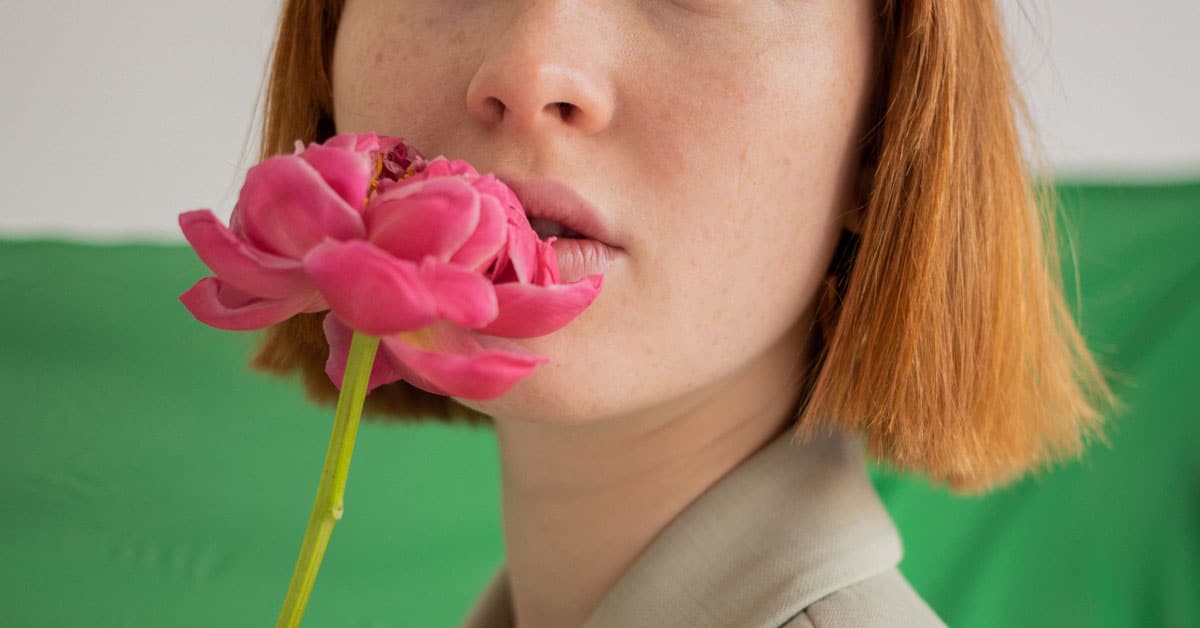 A woman holds a flower up to her pursed lips