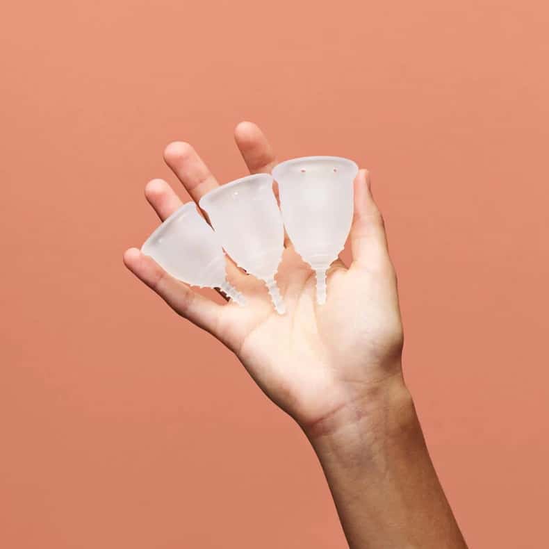 A womans hand holds up three different sizes of All Matters Menstrual Cups