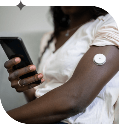 Black woman holding her cellphone looks at data from the continuous glucose monitoring she is wearing