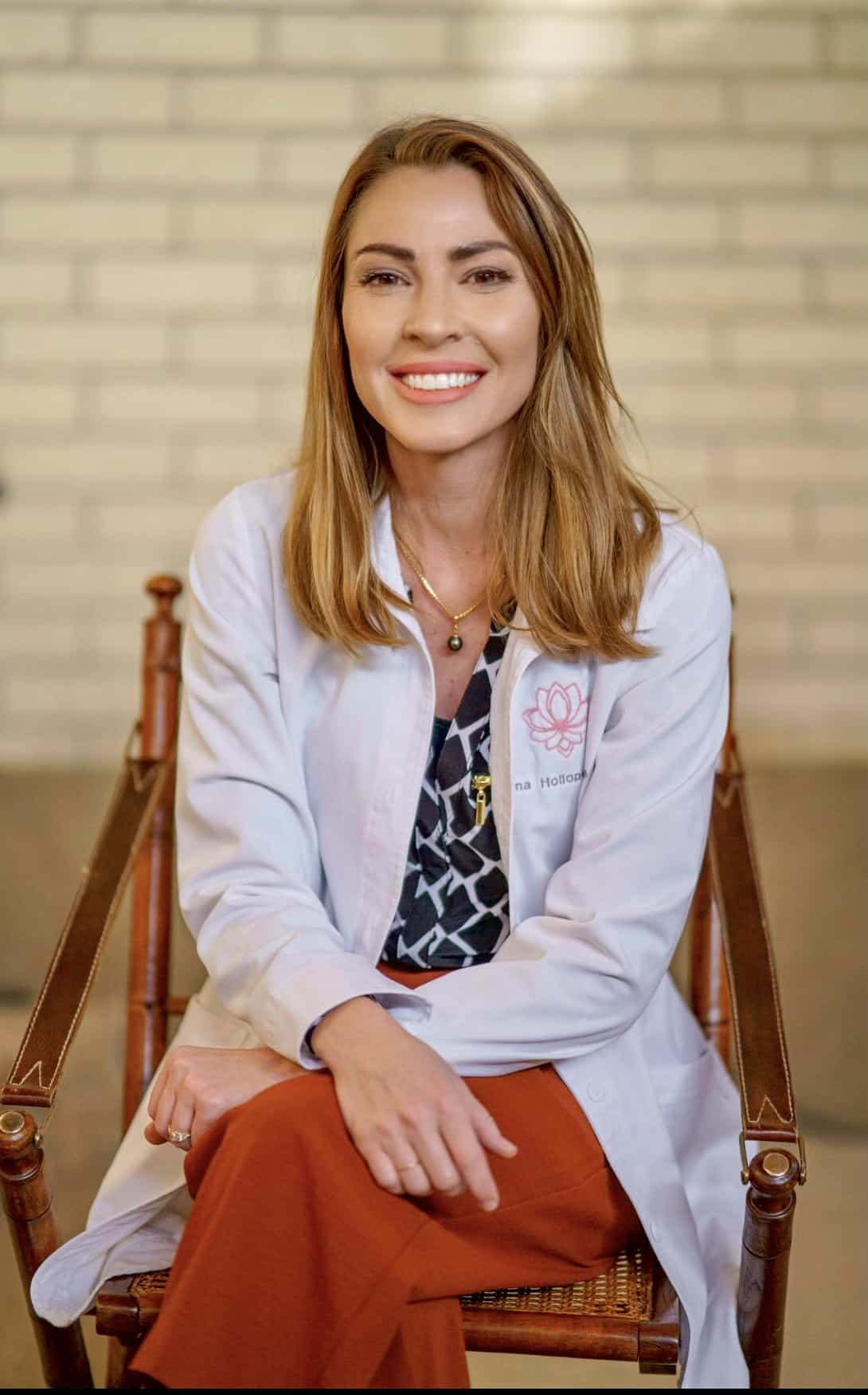 Dana sits in a white Aviva Lab Coat on a chair with a brick background.